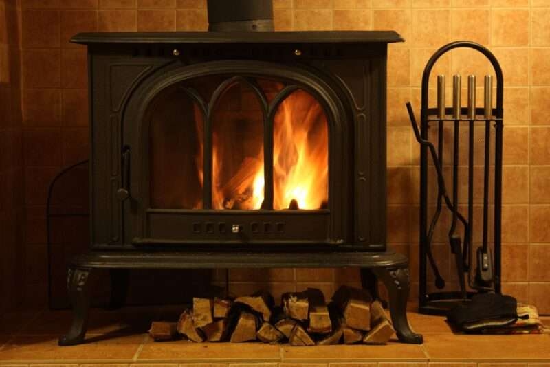 wood stove with fire burning inside and logs underneath